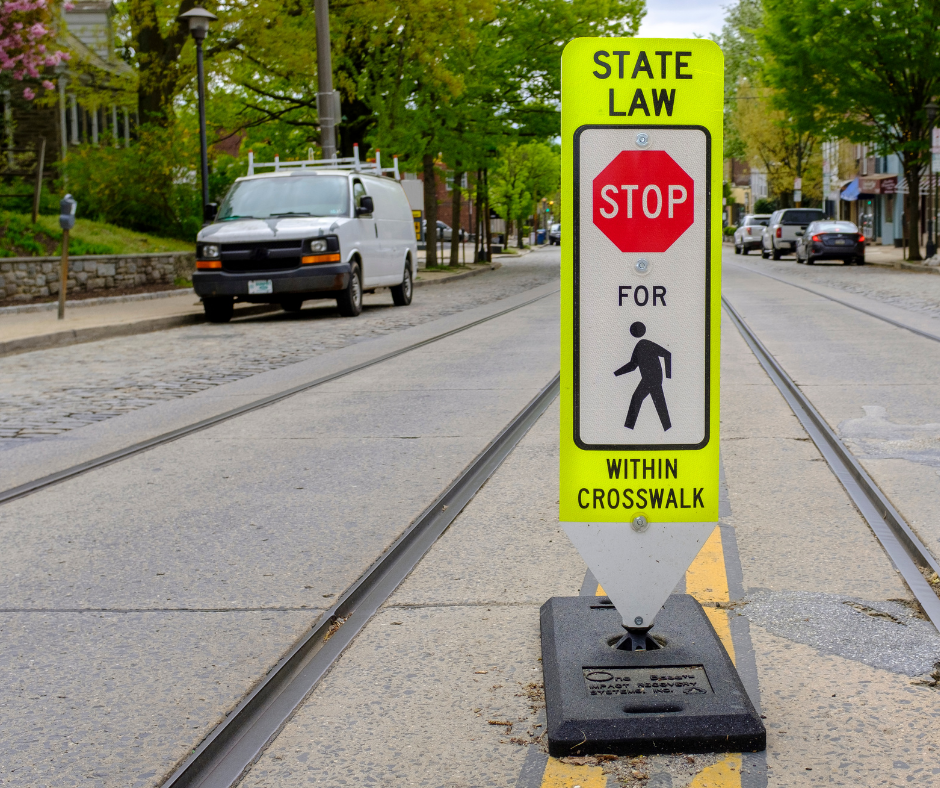 Sign that says "State Law Stop for [pedestrian] within crosswalk" on a street