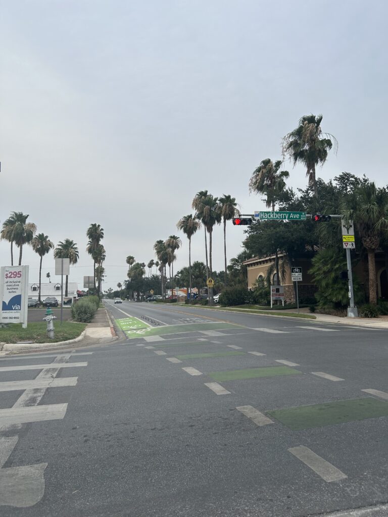 A photo of an intersection with a green painted bike lane with a bike box at the intersection. The traffic light arm has a street sign that says "Hackberry Ave."